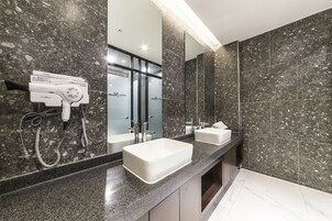Un baño moderno con encimeras de granito, dos lavabos, un secador de pelo y un espejo grande.