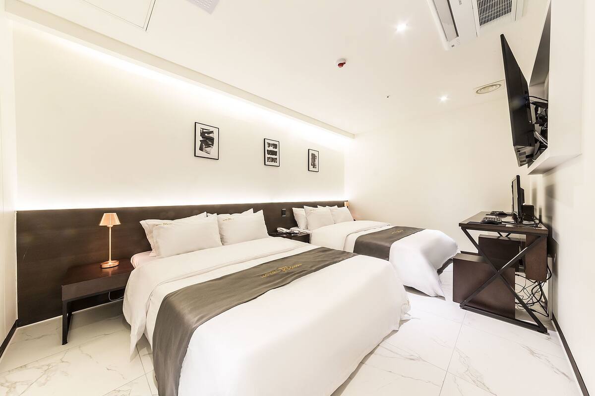 A modern hotel room with two beds, a desk, and a flat-screen TV.
