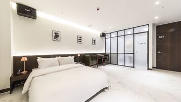 Una habitación de hotel moderna con una cama grande, un escritorio con silla, una mesita y un ventanal con paneles de vidrio esmerilado.