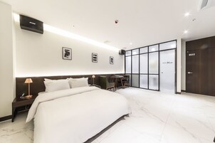Una habitación de hotel moderna con una cama grande, un escritorio con silla, una mesita y un ventanal con paneles de vidrio esmerilado.