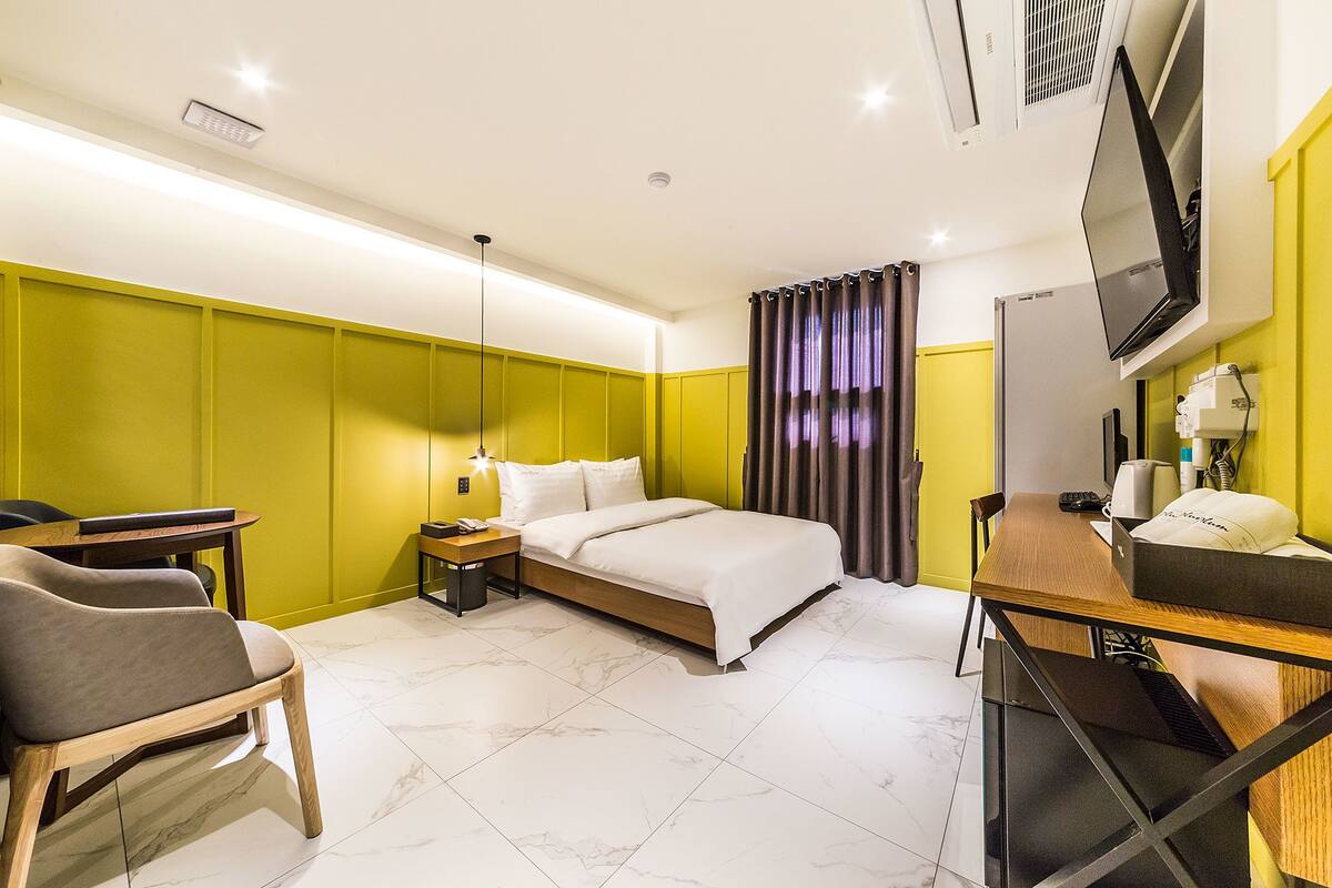 A modern hotel room with a bed, bedside table, chair, desk, and a TV.