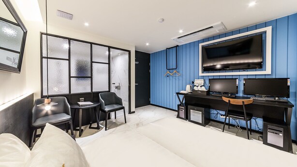 A modern bedroom with a bed, two chairs, a desk, a TV, and a wardrobe. - Hotel Plum (Siheung)