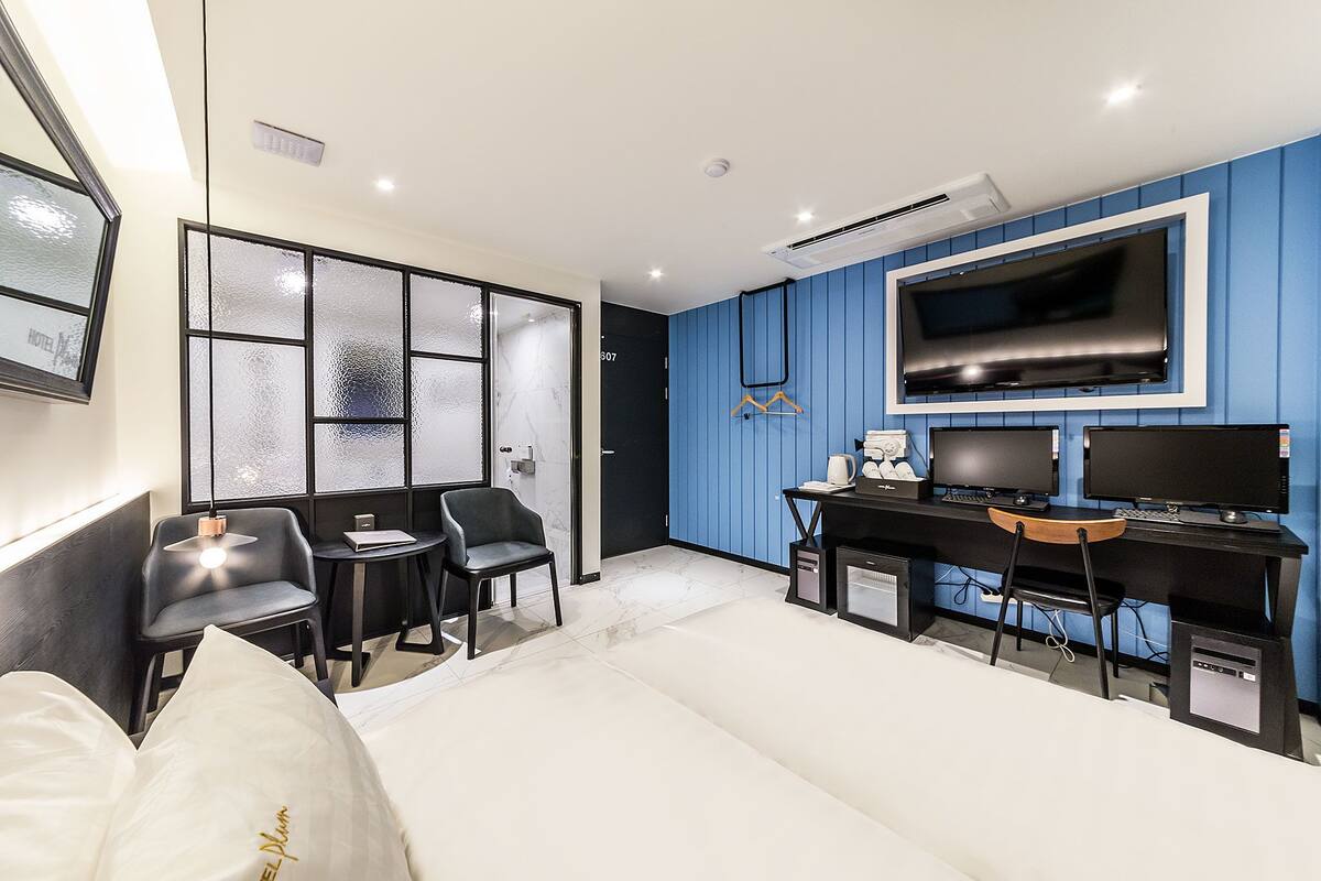 A modern bedroom with a bed, two chairs, a desk, a TV, and a wardrobe.