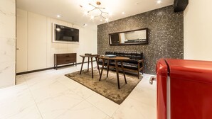 A modern hotel room with a large TV, a sofa, a dining table, and a red suitcase. - Hotel Plum (Siheung)