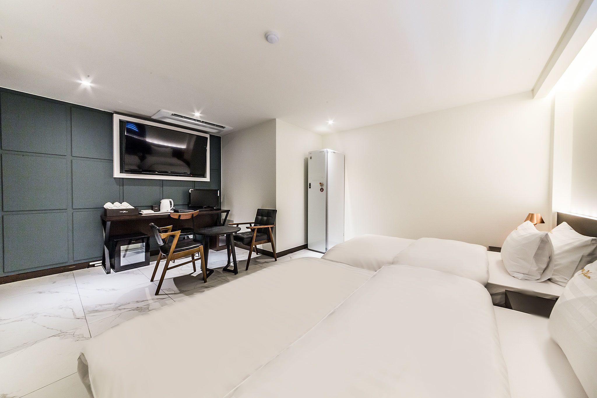 A modern hotel room with a large bed, a desk with a chair, a television, and a wardrobe.