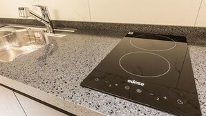 A kitchen with a black induction cooktop and a stainless steel sink. - Hotel Plum (Siheung)