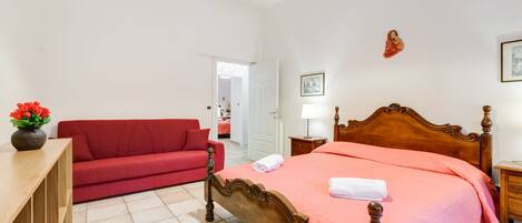 Una habitación de hotel con una cama de madera, un sofá rojo, una mesita de noche de madera y un jarrón con flores.