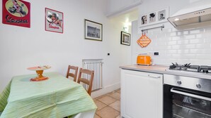 A compact kitchen with a dining table, chairs, a radiator, a stove, and a small oven. - Domus Ricca Termini (Rome)