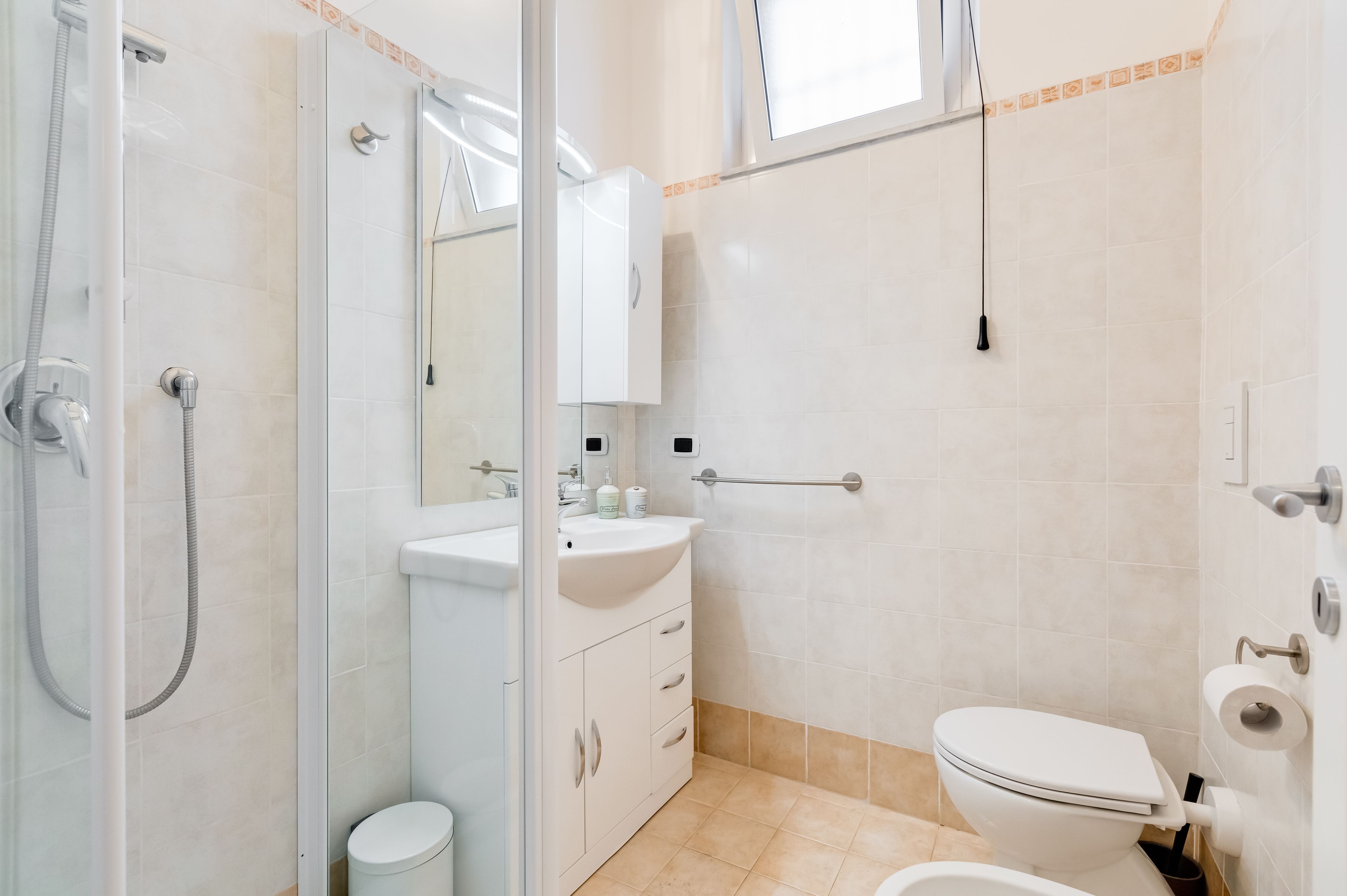 Ein modernes Badezimmer mit Duschkabine aus Glas, Waschbecken in Weiß mit Spiegel und Toilette.