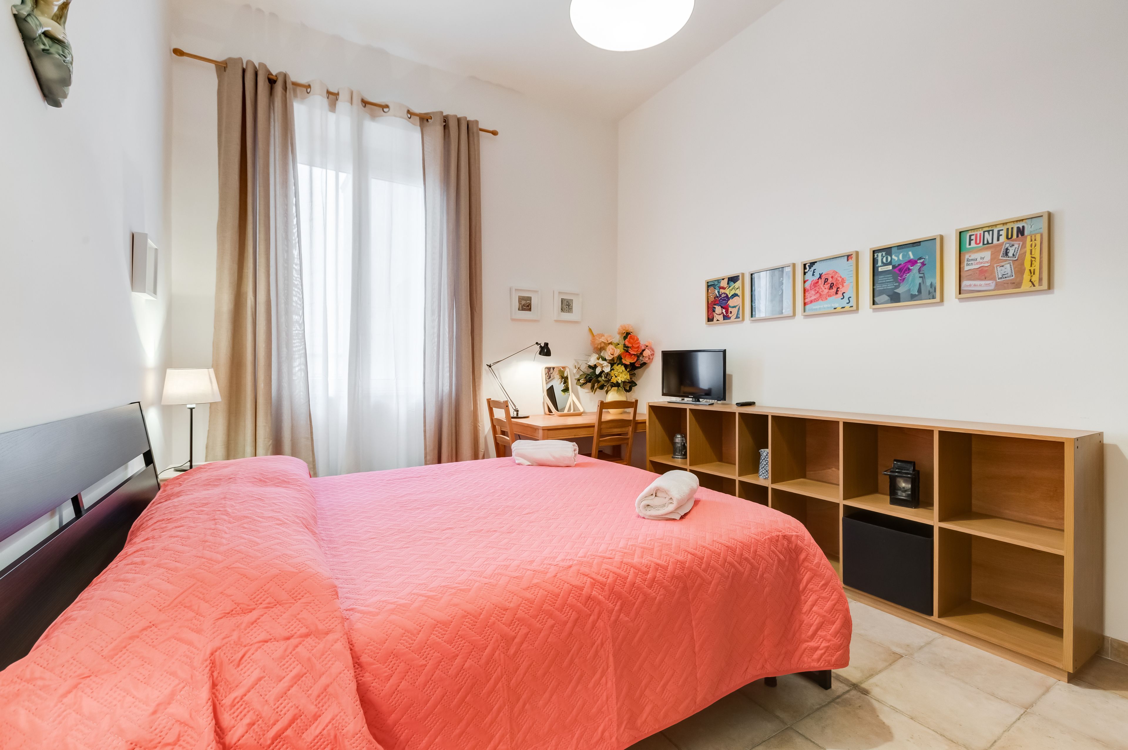 Une chambre d’hôtel avec un grand lit, un bureau avec une chaise, une télévision et une étagère avec des boîtes de rangement.