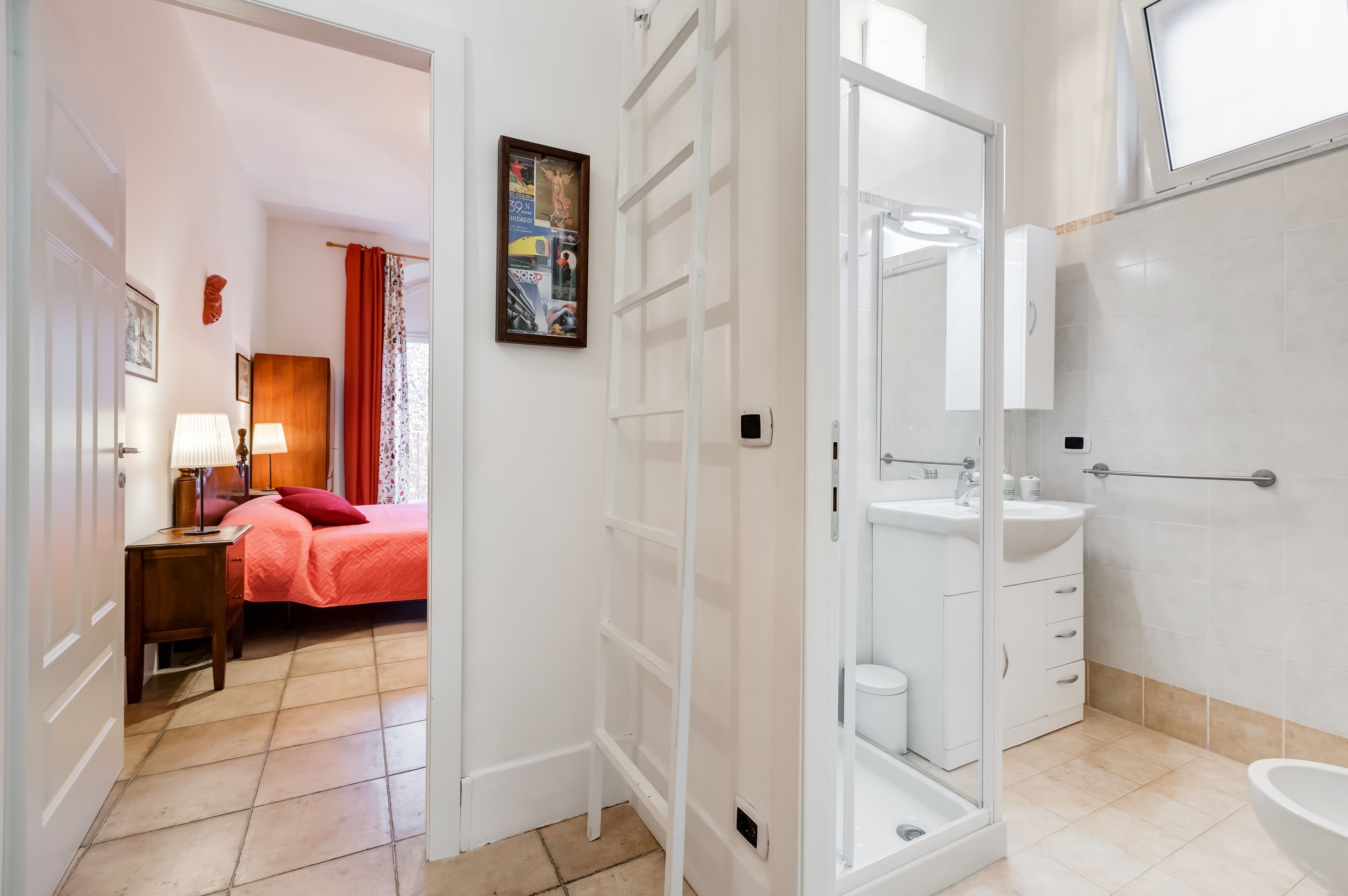 A hotel room with a bed, a nightstand, a lamp, a painting, and a bathroom with a sink and toilet.