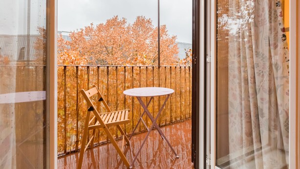 A balcony with a wooden chair and a small round table, a bamboo fence, and a view of autumn trees. - Domus Ricca Termini (Rome)