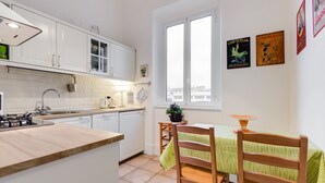 A modern kitchen with white cabinets, a wooden countertop, and a dining area with a green-striped tablecloth. - Domus Ricca Termini (Rome)
