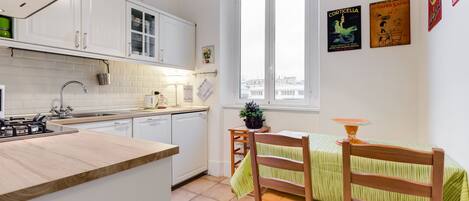 A modern kitchen with white cabinets, a wooden countertop, and a dining area with a green-striped tablecloth.