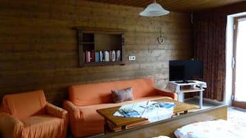 A cozy room with a wooden ceiling, a sofa, a television, and a bookshelf.