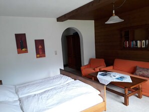 Una habitación con una cama, una mesa de madera con una revista, un sofá naranja y una estantería.