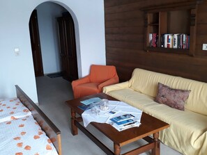 A room with a wooden table, a sofa, a bookshelf, and a door leading to another room. - Double Room (Type A) - Greber Christine - Frühstückspension Fernblick (Schoppernau)