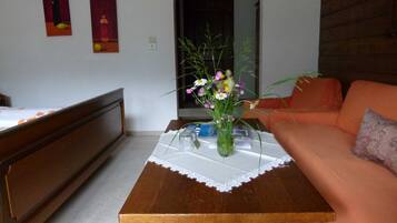 A room with a wooden table, a vase with flowers, a sofa, and a bed.
