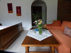 Ein Zimmer mit einem Holztisch, einem Blumenvasen, einer Couch und einem Bett.