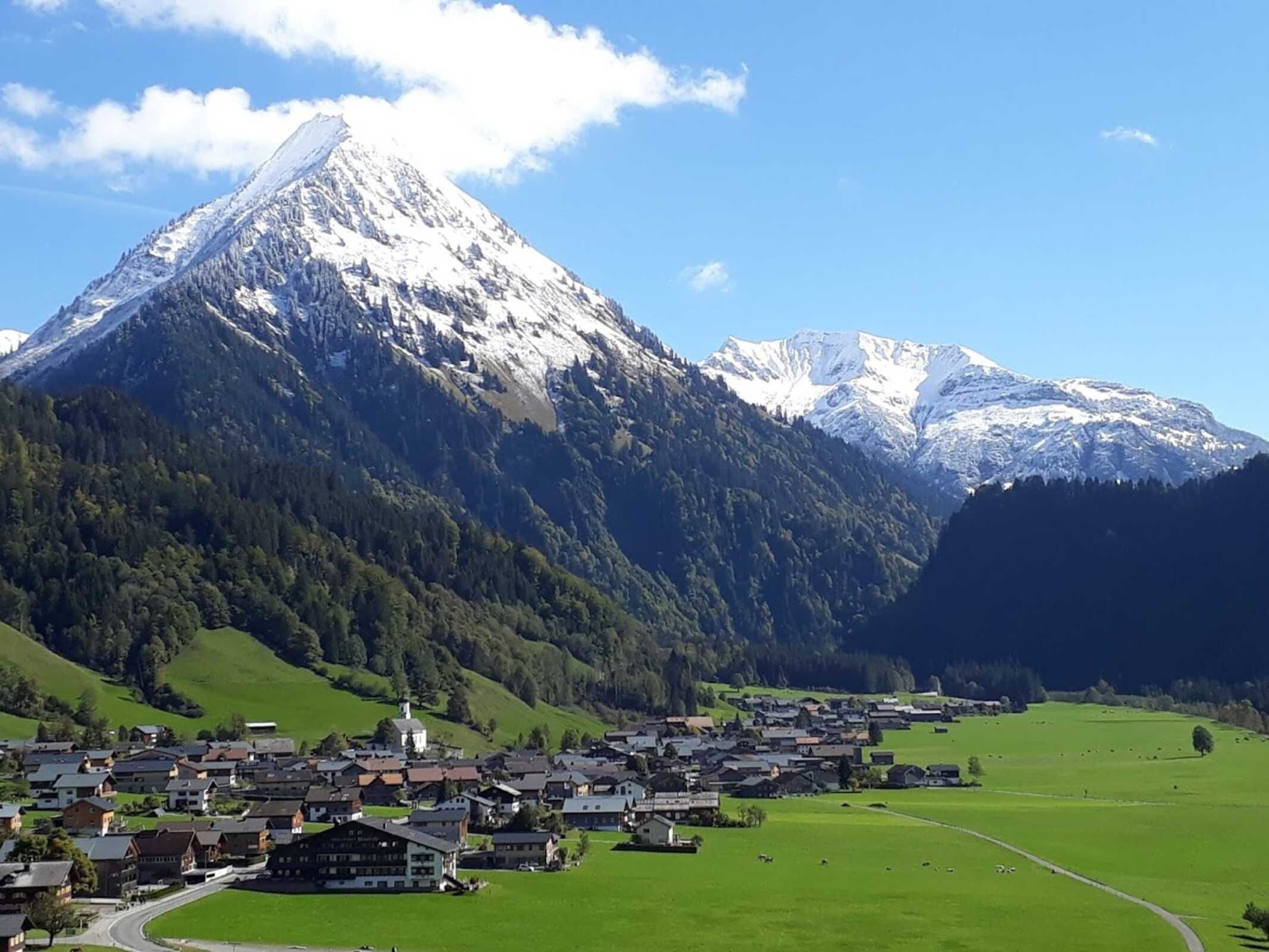 Une ville de montagne dominée par un sommet enneigé, entourée de prairies verdoyantes et regroupant un ensemble de bâtiments traditionnels.