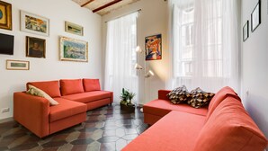 A living room with two red sofas, a coffee table with a plant, and a large window with sheer curtains. - Monti Colosseum Apartment-Urbana (Rome)