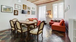A dining area with a wooden table and chairs, a red sofa, and artwork on the walls. - Monti Colosseum Apartment-Urbana (Rome)