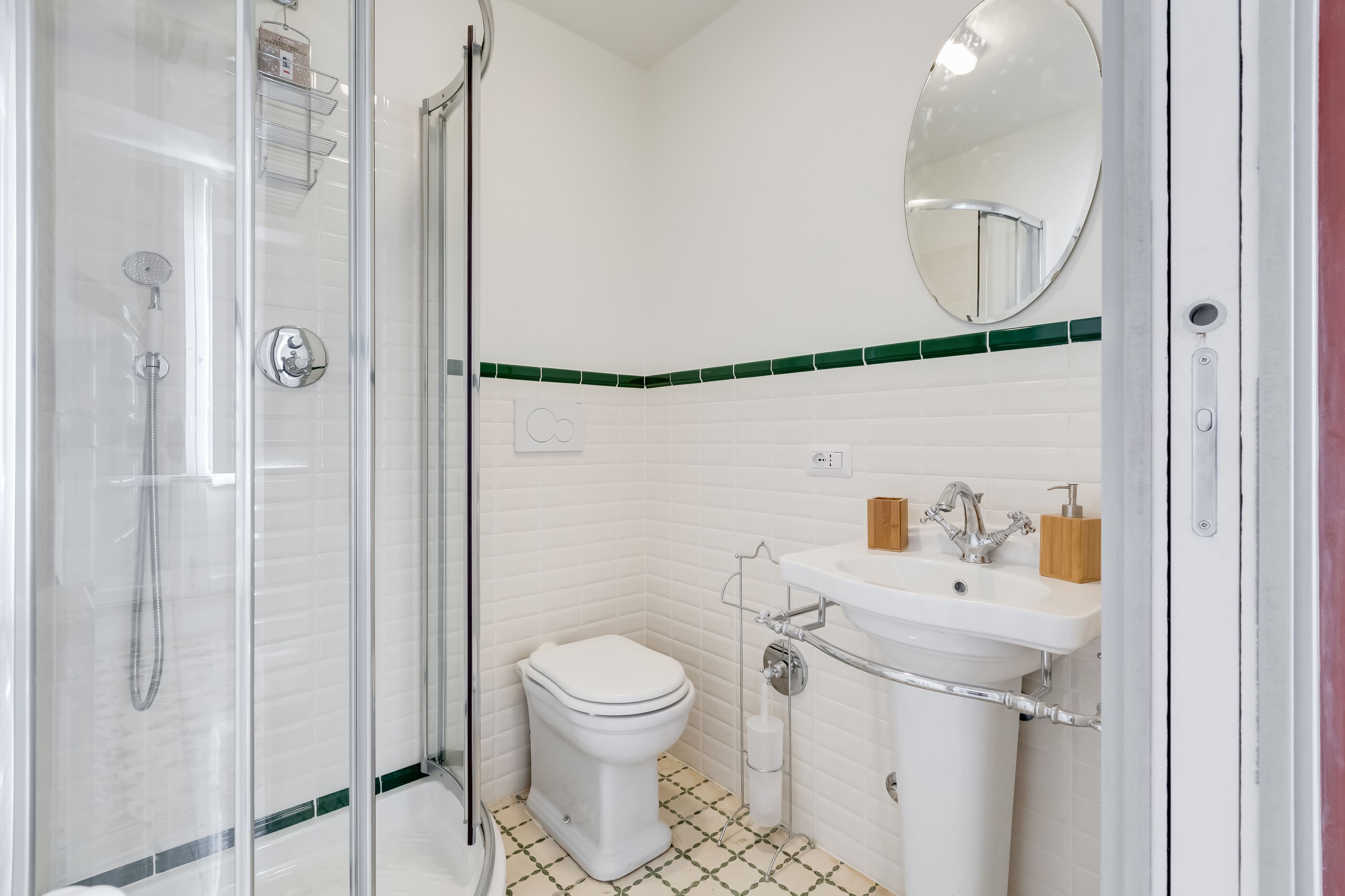 A bathroom with a glass-enclosed shower, a white toilet, a sink with a mirror, and green-tiled walls.