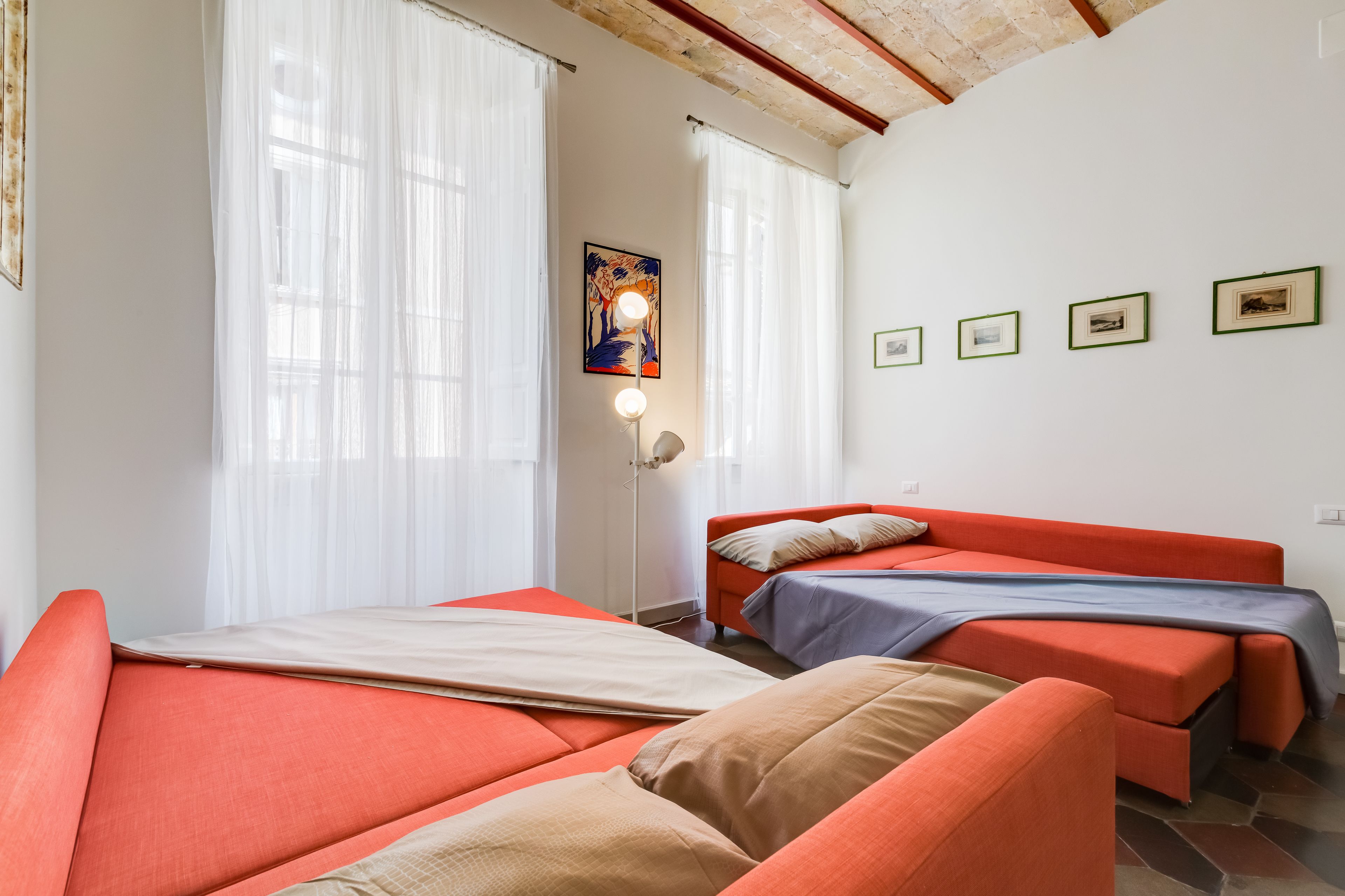 A room with two beds, a standing lamp, and a painting on the wall.