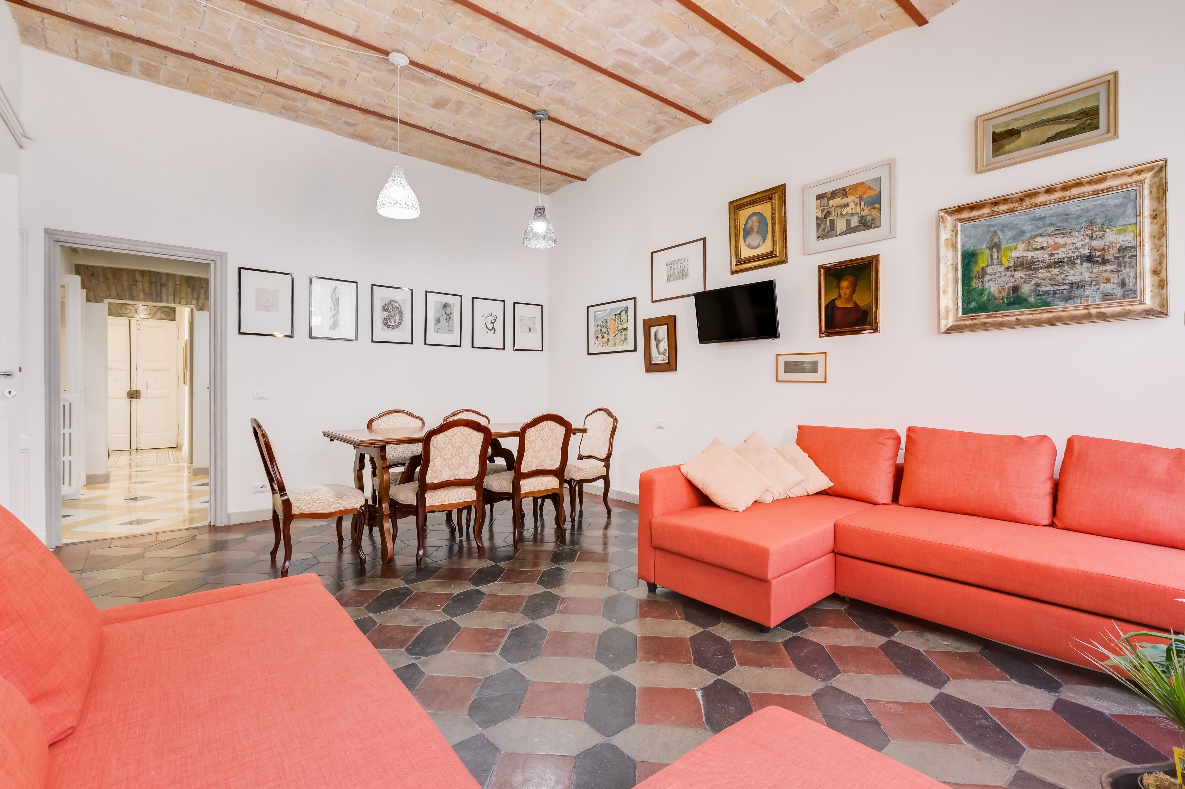 Una sala de estar con un sofá rojo, una mesa de comedor con sillas y un televisor montado en la pared.