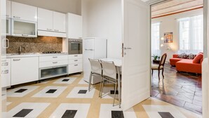 A modern kitchen with white cabinets, a stainless steel range, and a dining area with a white table and chairs. - Monti Colosseum Apartment-Urbana (Rome)