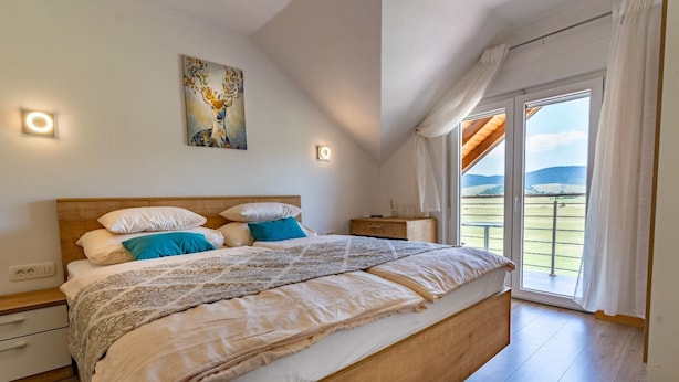 Une chambre à coucher avec un grand lit, une table de chevet, une lampe fixée au mur et une fenêtre avec des rideaux.
