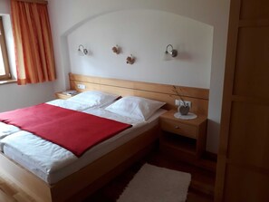 Ein Bett mit weißer Bettwäsche, einer roten Decke und einem hölzernen Kopfteil. Es gibt zwei Nachttische mit Lampen und einen Beistelltisch.