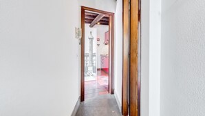 A narrow hallway with a wooden door leading to a room with a tiled floor and a red wall. - Romantic House in Trastevere (Rome)