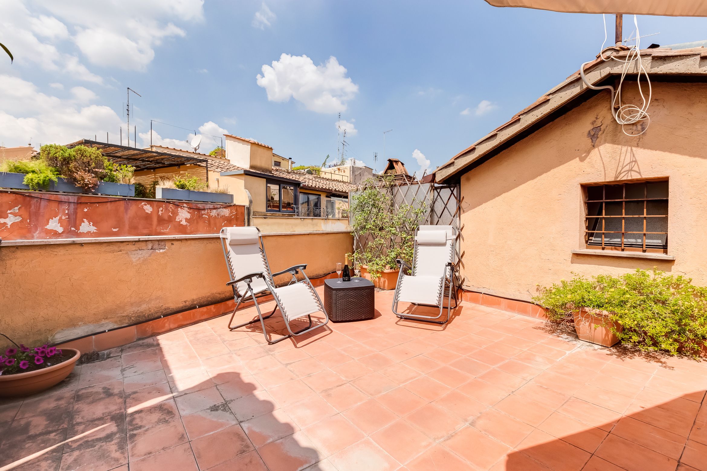 A rooftop patio with two white lounge chairs, a small round table, and potted plants.