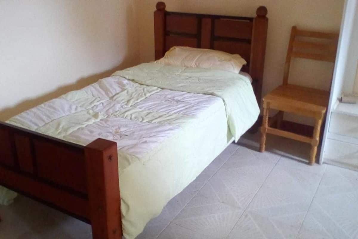 A single bed with a wooden frame and a simple headboard, accompanied by a wooden chair.
