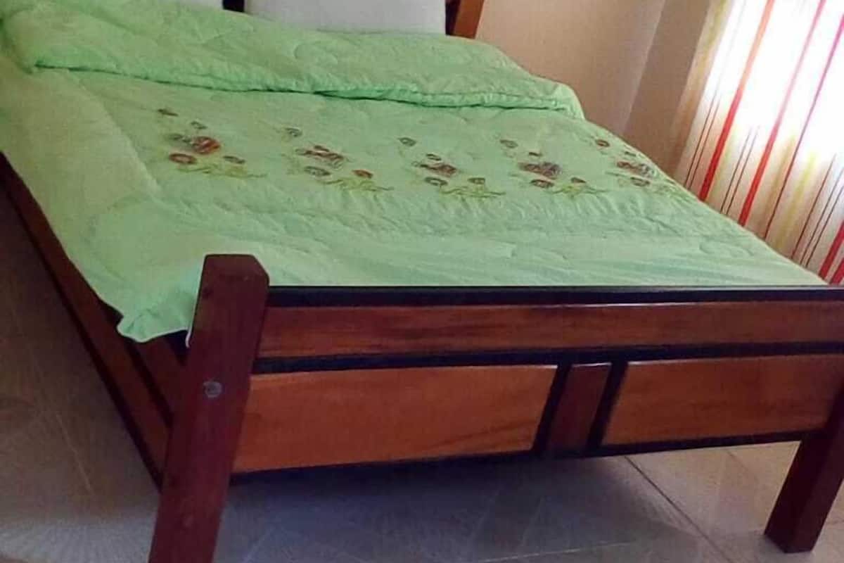 A wooden bed with a green bedspread and two pillows in a room with tiled flooring.