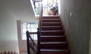 A staircase with a handrail, a potted plant on the landing, and a window with a metal grille. - Rose House Hotel (Ngong)