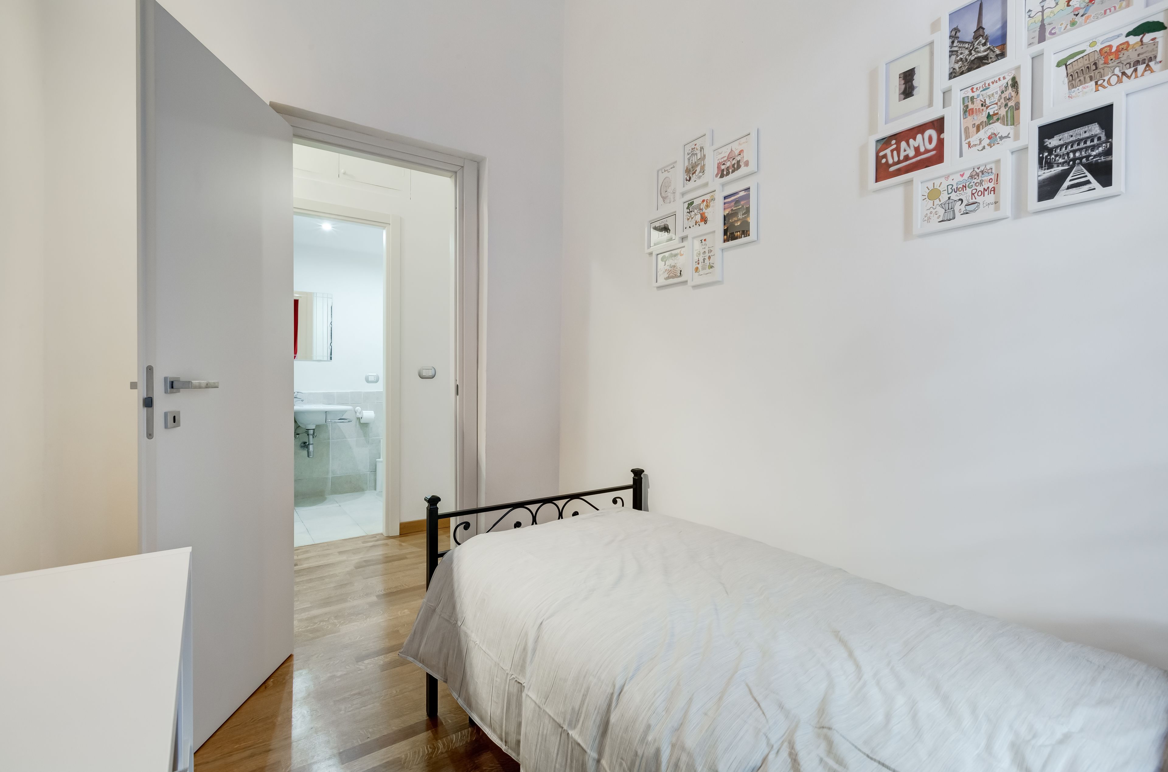 A bedroom with a bed, a door leading to a bathroom, and a wall with framed pictures.