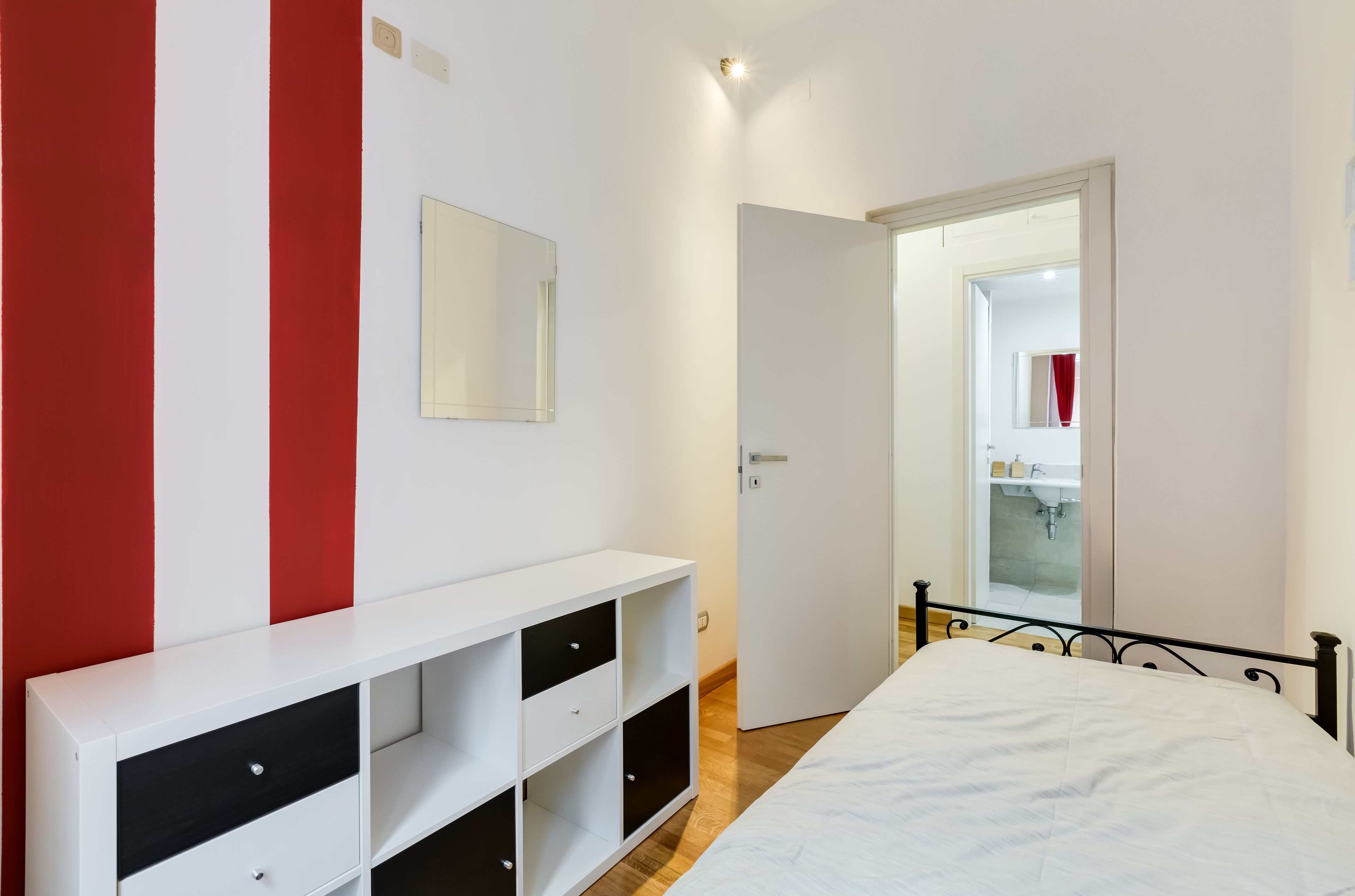 A bedroom with a bed, a white console table with drawers, a mirror, and a door leading to a bathroom.