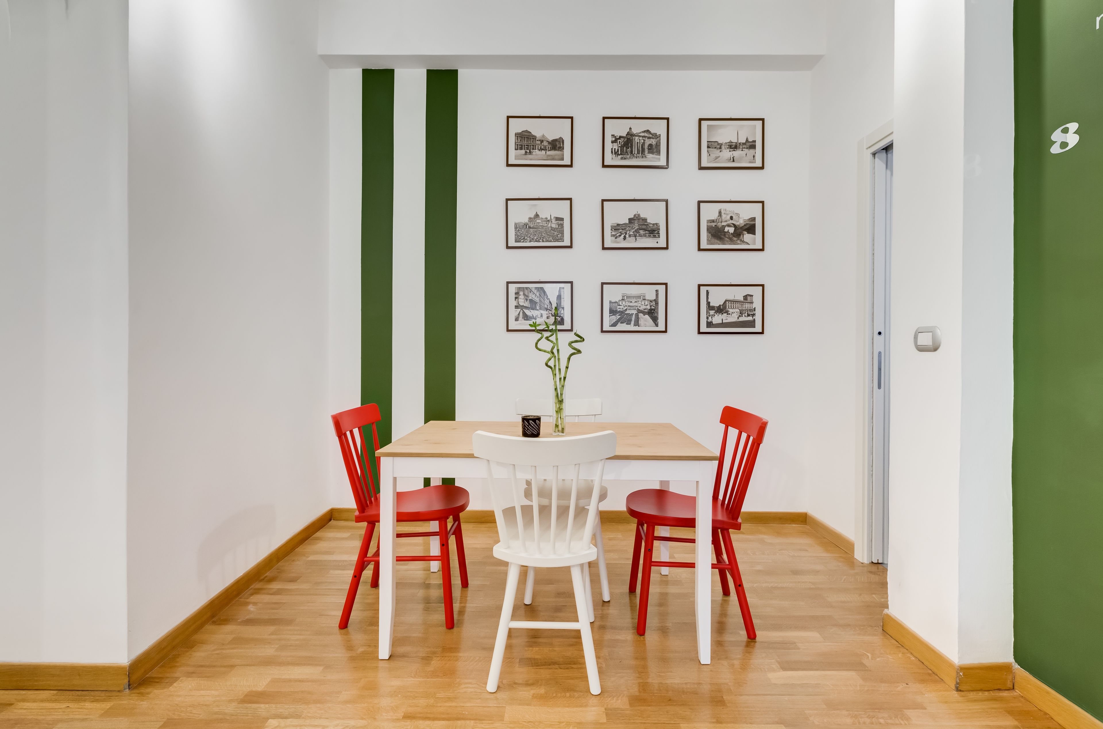 A dining area with a wooden table and four red chairs, a green stripe on the wall, and framed pictures above the table.