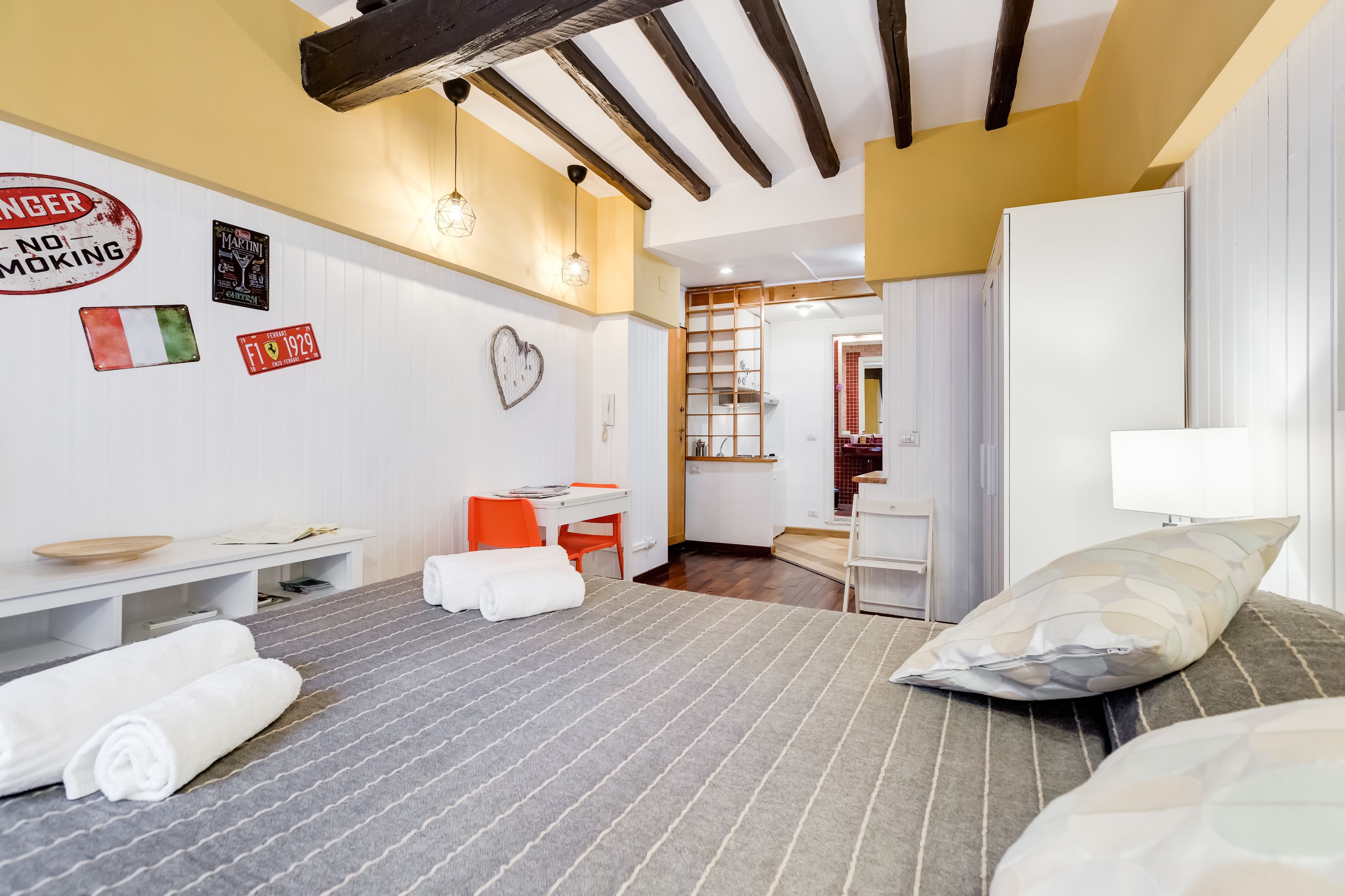 Habitación de hotel con cama, escritorio, silla y armario. Hay toallas sobre la cama y un cartel en la pared.