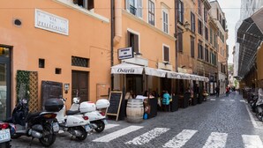A cobblestone street lined with buildings, outdoor seating at cafes, and parked scooters. - Pellegrino Campo de' Fiori Suite (Rome)