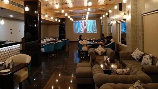 A spacious lobby with a high ceiling, wooden beams, and pendant lighting. There is a seating area with sofas and a bar with a counter. - Hotel Grand Maple (Jaipur)