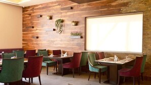 A restaurant with a rustic wooden wall, multiple dining tables with chairs, and a large window providing natural light. - Hotel Grand Maple (Jaipur)