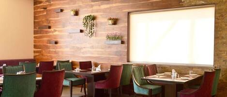 A restaurant with a rustic wooden wall, multiple dining tables with chairs, and a large window providing natural light.