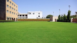 A large, open grassy area with a building in the background. - Hotel Grand Maple (Jaipur)