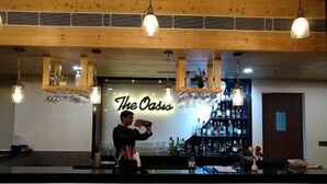 A bar area with a sign reading "The Oasis," a bartender, and a bar stocked with bottles. - Hotel Grand Maple (Jaipur)