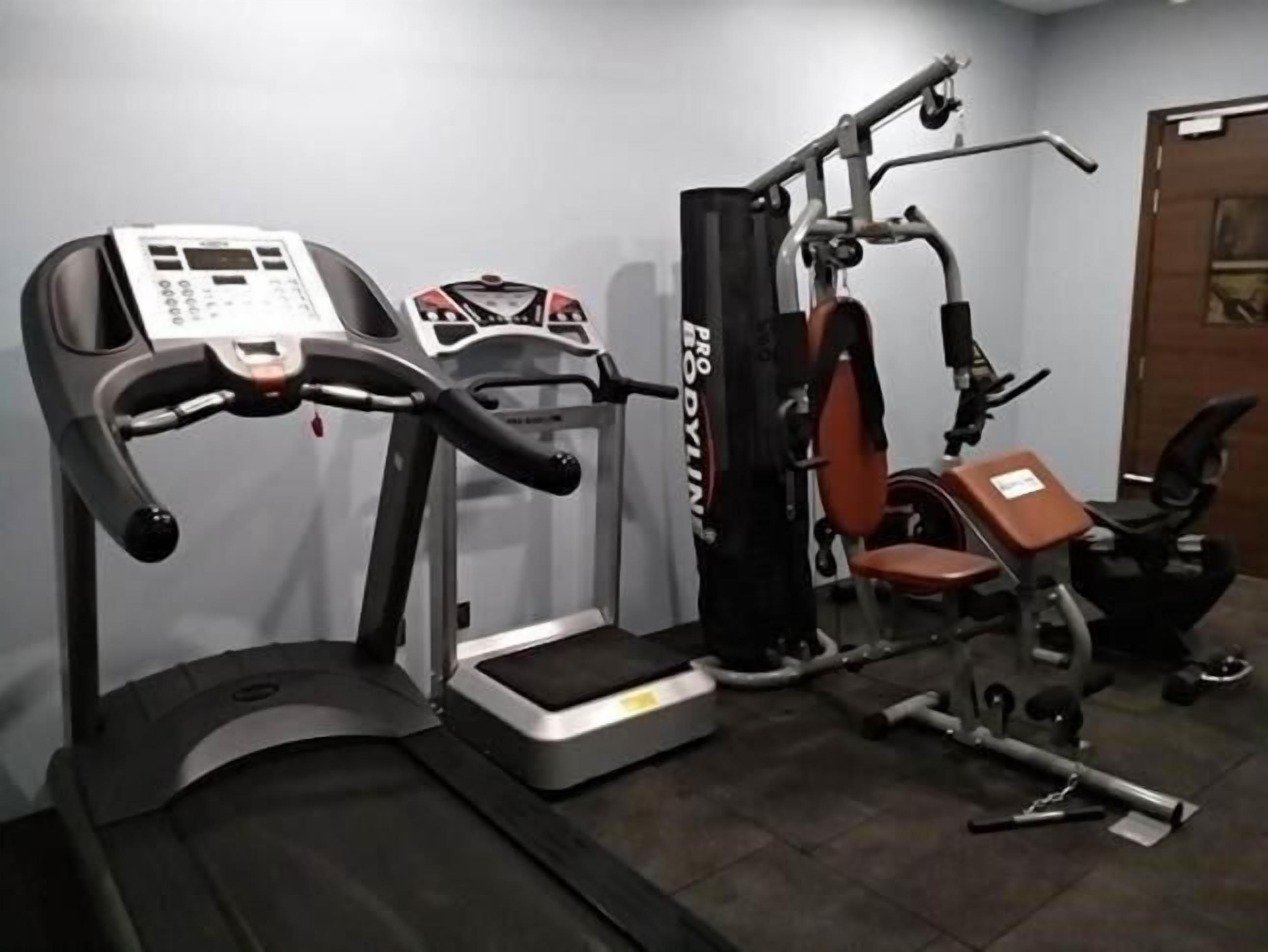 Un gimnasio con cinta de correr, máquina de pesas y banco.