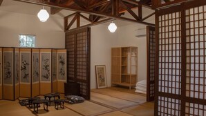 Ein traditioneller japanischer Raum mit Tatami-Bodenbelag, Shoji-Schirmwänden, einem niedrigen Holztisch mit Kissen und hängenden Papierlaternen.
