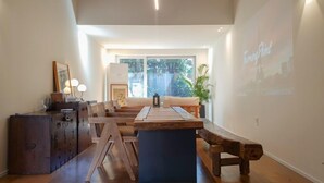 Ein modernes Wohnzimmer mit einem Holzesstisch, einer Couch und einer Projektionsleinwand, auf der eine Stadtansicht zu sehen ist.